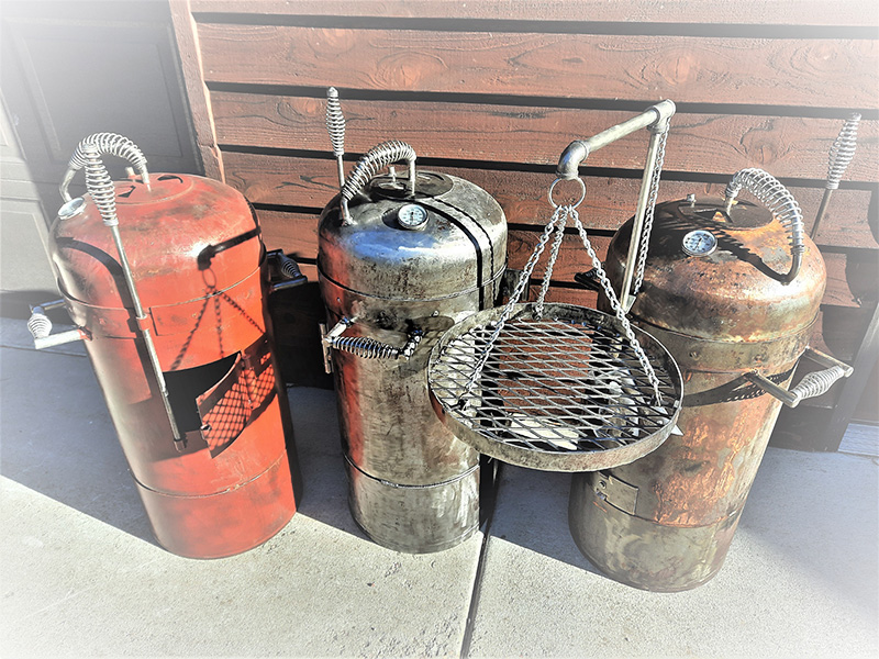 Three Bullet grills: red, silver, and rust. One with hanging grill grate suspended on a swing arm