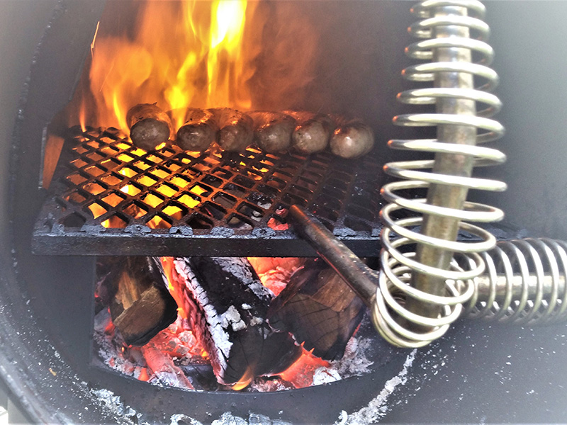 Close-up inside firebox, sausages on the grill over flaming embers.