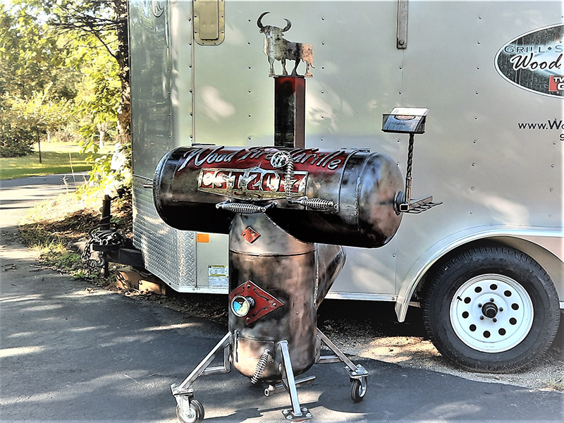 T-shaped black grill with red & silver artwork saying Woodfired Grille Est. 2017