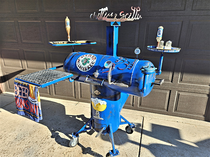 Blue T-shaped grill with grate rack & towel holder in front. Two accessory arms. Logo Pabst Milwaukee 