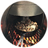 Close-up of cast iron skillet w/ sliced mushrooms on grate inside grill over glowing embers.